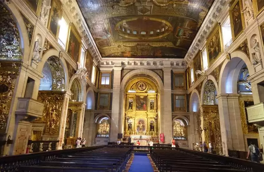 Durante o dia, interior da Igreja de São Roque com várias pinturas e bancos de madeira