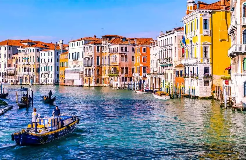 durante o dia, pessoas passeando em gôndolas em um dos canais de veneza, rodeado por edifícios coloridos