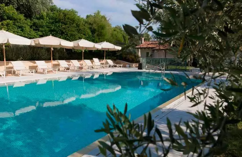 Durante o dia, árvores, espreguiçadeiras e guarda-sóis ao redor de grande piscina ao ar livre em um dos melhores hotéis em verona