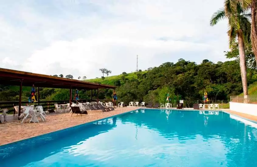Durante o dia, árvores, espreguiçadeiras e mesas ao redor de piscina ao ar livre em hotel fazenda no Brasil