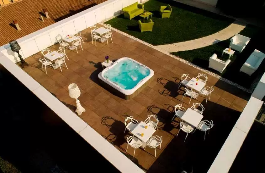Durante dia de sol, vista aérea de um hotel em verona com jacuzzi no centro, e mesas, cadeiras, luminárias, sofás e área gramada em volta