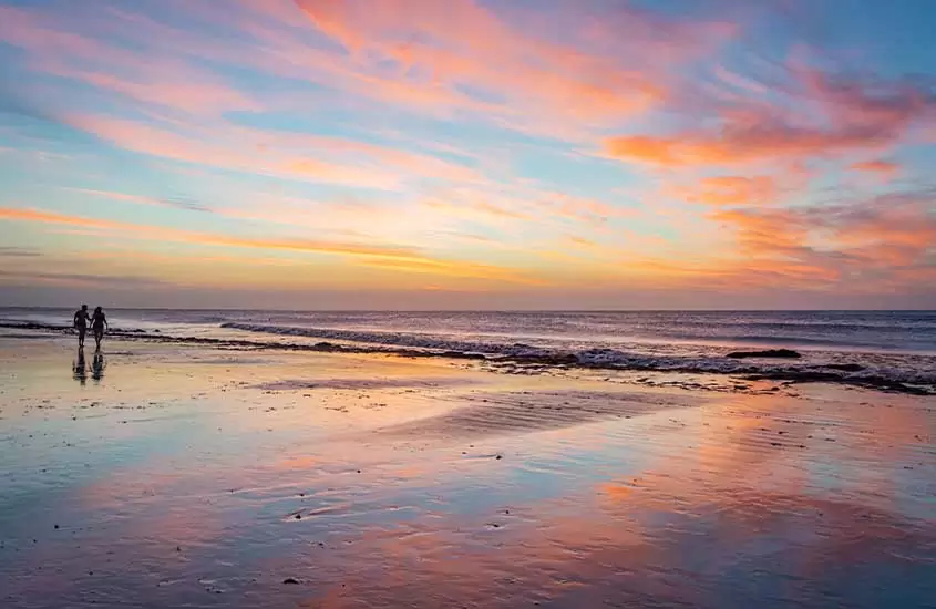 vista panorâmica do nascer do sol refletido na areia e dois banhistas a esquerda em Jericoacoara