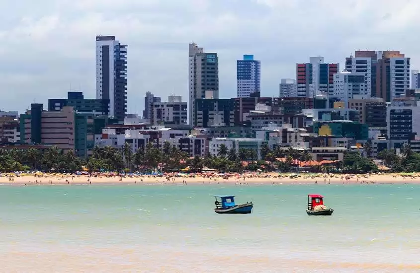 em dia de sol, vista panorâmica de dois barcos coloridos em mar de João Pessoa. Ao fundo, diversos prédios