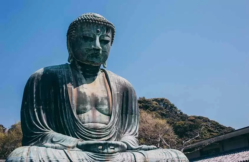 Durante um dia de sol, estátua de Buda de cerca de 13,35 metros, com algumas árvores atrás