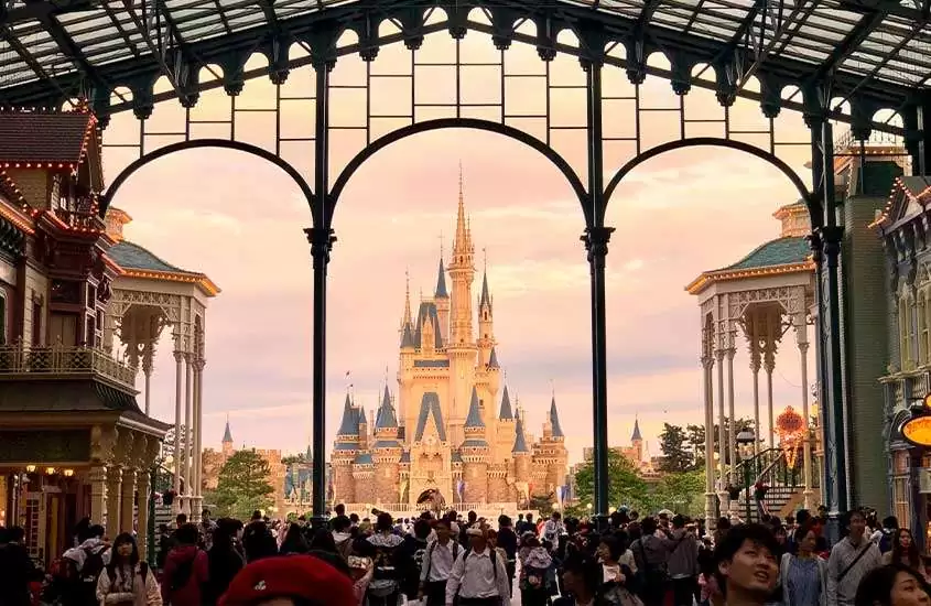 Em dia de sol, pessoas caminhando em frente a castelo em Disneyland Tokyo, um dos pontos turísticos do japão