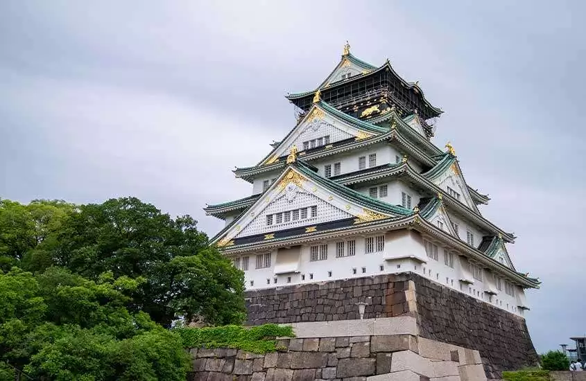 Em dia nublado, árvores à esquerda de imponente castelo de osaka, um dos principais pontos turísticos do japão