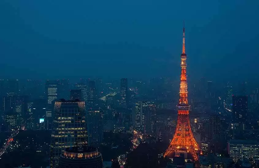 Durante a noite Tokyo Tower, torre inspirada na torre eiffel, iluminada com vários prédios ao redor