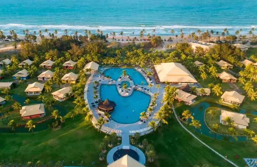 Em dia de sol, vista aérea panorâmica de um dos melhores resorts all inclusive no brasil para lua de mel com piscinas, rodeadas por árvores à beira-mar