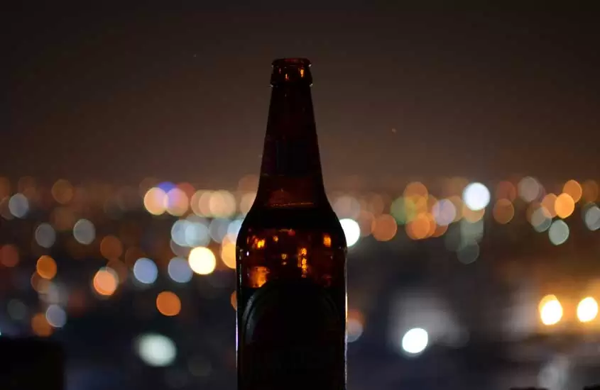 Durante a noite, garrafa de cerveja iluminada pelas luzes da cidade