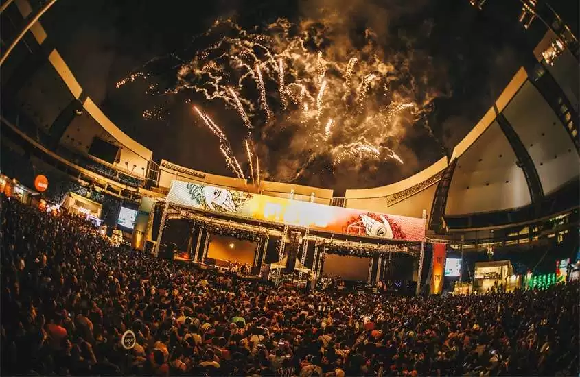 Durante a noite, pessoas assistindo show de fogos e show em um dos festivais de música no brasil
