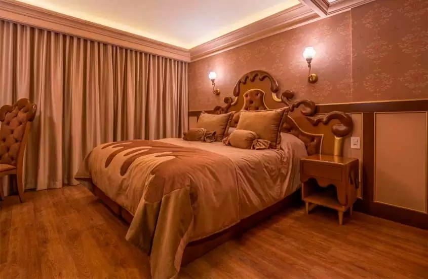 Quarto de hotel com móveis inspirandos em chocolate derretendo, incluindo cama, mesa de cabeceira e cadeira. Ao fundo, janela grande acortinada
