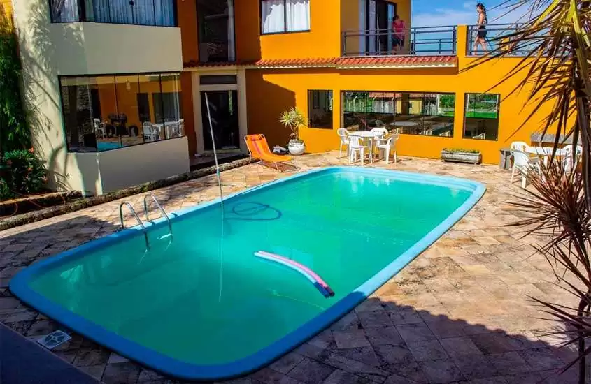 Em dia de sol, mesas e cadeiras ao redor de piscina em quintal de casa de temporada para o réveillon florianópolis 2024