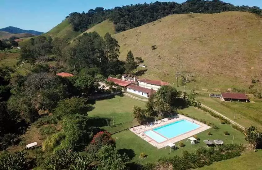 Em dia de sol, vista aérea panorâmica de resort all inclusive no Rio de Janeiro com piscina, rodeada por árvores e montanhas