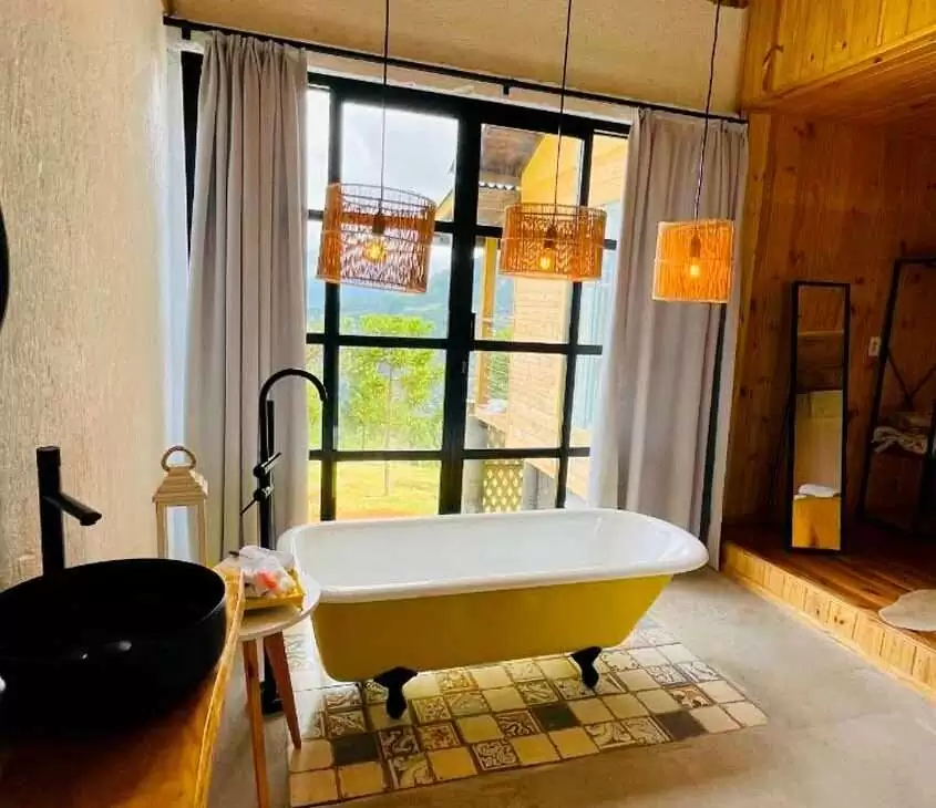 Em dia nublado, banheiro de um chalé romântico em santa catarina com banheira, lustres decorativos, toalhas espelhos, tapete de pele e janelas grandes acortinadas