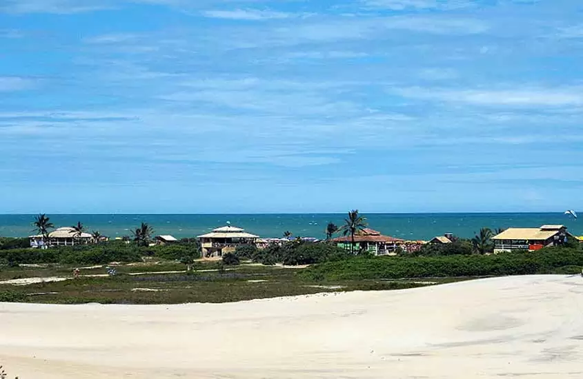 Em dia de sol, vista panorâmica de quiosques e coqueiros à beira-mar