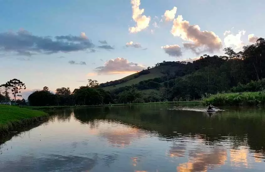 Durante um fim de tarde, lago com jetsky, montes gramados e árvores ao redor