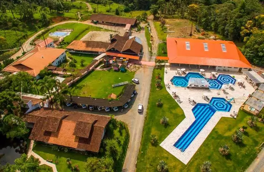 Em dia de sol, vista aérea de piscinas, carros, construções, árvores e áreas gramadas em um hotel fazenda no Brasil