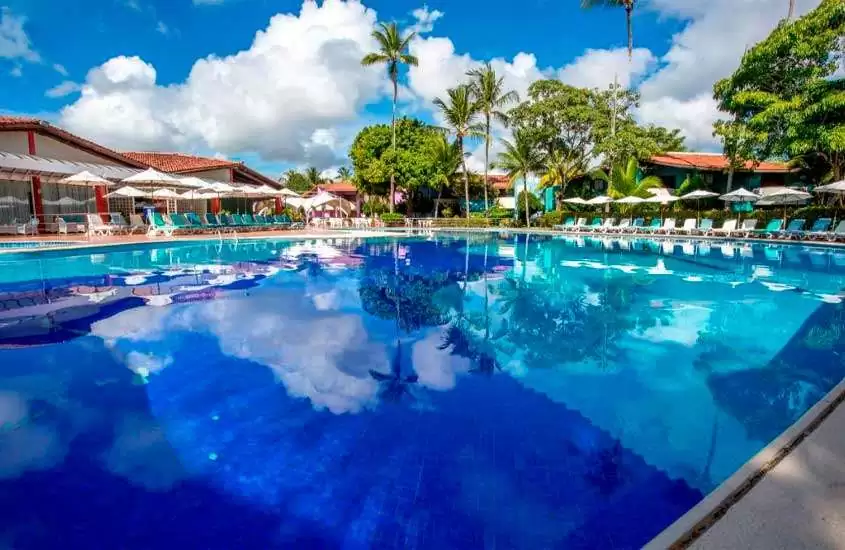 Em dia de sol, árvores ao redor de piscina em área de lazer ao ar livre de um dos melhores resorts all inclusive no brasil para lua de mel