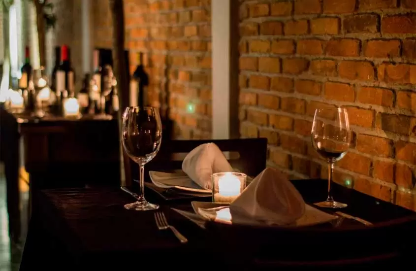 Restaurante de um hotel para comemorar aniversário de casamento com mesas postas, vinhos, taças e parede de tijolinhos