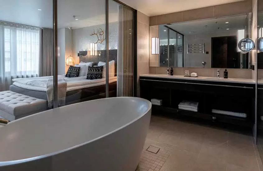 Quarto de hotel em helsinque com cama de casal, banheira, toalhas, 2 pias, espelho, luminárias e janela acortinada