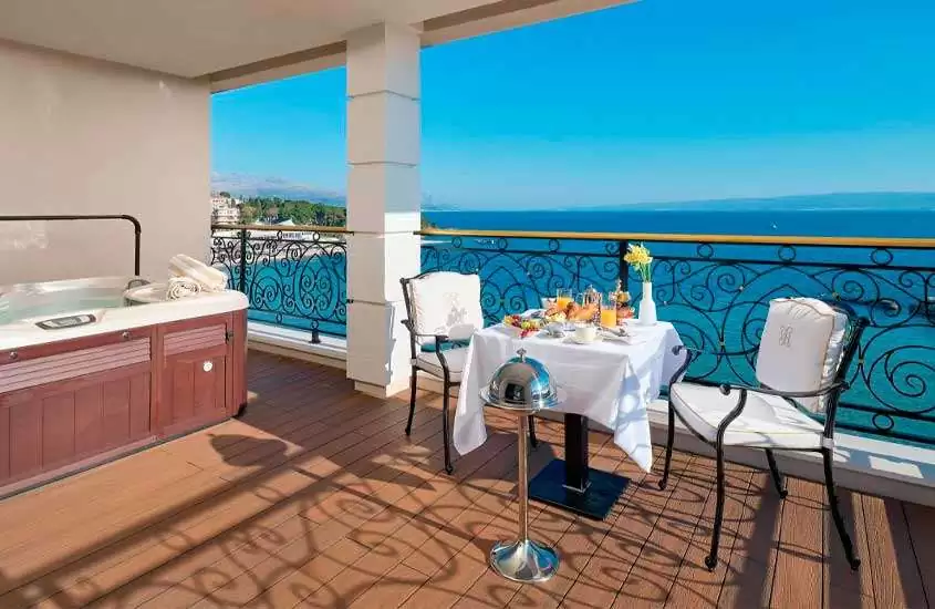Em dia de sol, varanda de suíte com banheira de hidromassagem, café da manhã servido em mesa e vista para o mar