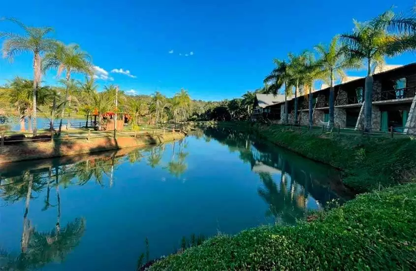 Em um dia de sol, um dos hotéis fazenda próximo a brasilia com lago na frente, parte gramada, arvores ao redor e hotel ao lado