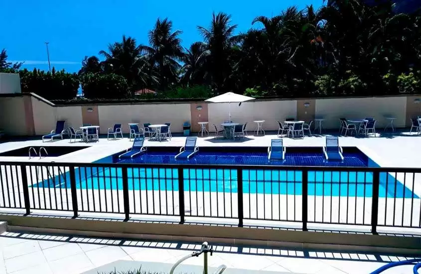 Em um dia de sol, área de lazer de um hotel na barra da tijuca beira-mar com piscinas, mesas, cadeiras, espreguiçadeiras e guarda-sol