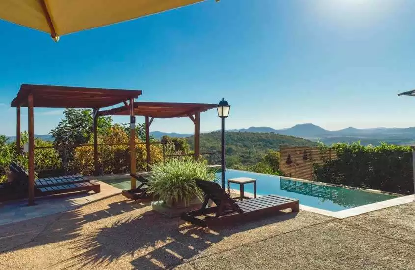 Em um dia de sol, área de lazer de um dos melhores hotéis fazenda proximo a brasilia com piscina, espreguiçadeiras de madeira, pergolados, flores e árvores decorativas