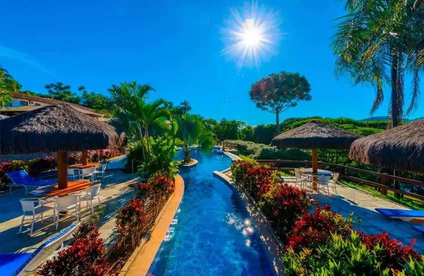Durante um dia de sol, área de lazer de um hotel fazenda perto de brasília com piscinas, mesas, cadeiras, espreguiçadeiras, flores e árvores decorativas
