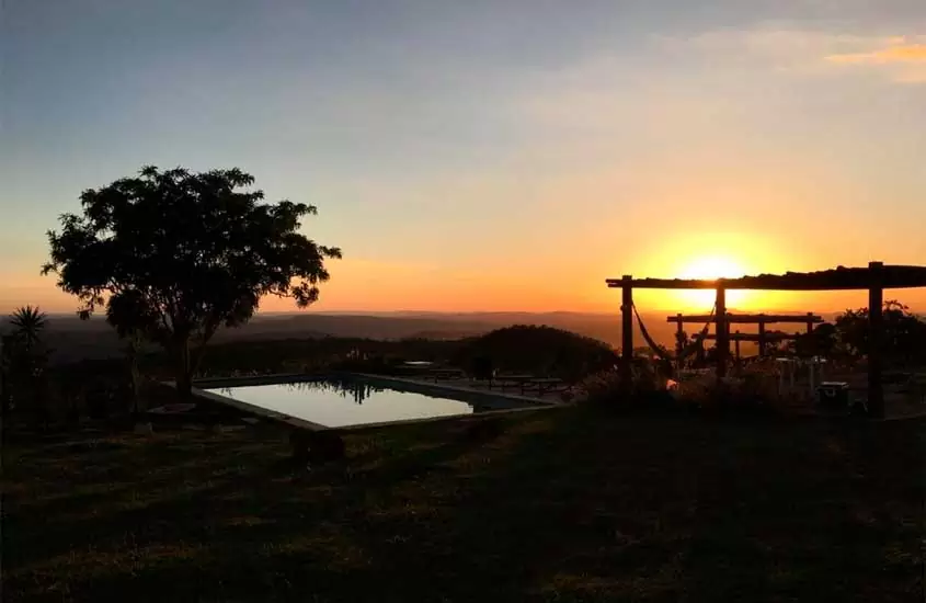 Durante o pôr do sol, área de lazer de um dos hotéis fazenda proximo a brasilia df com piscina, pergolados, árvores, redes e parte gramada