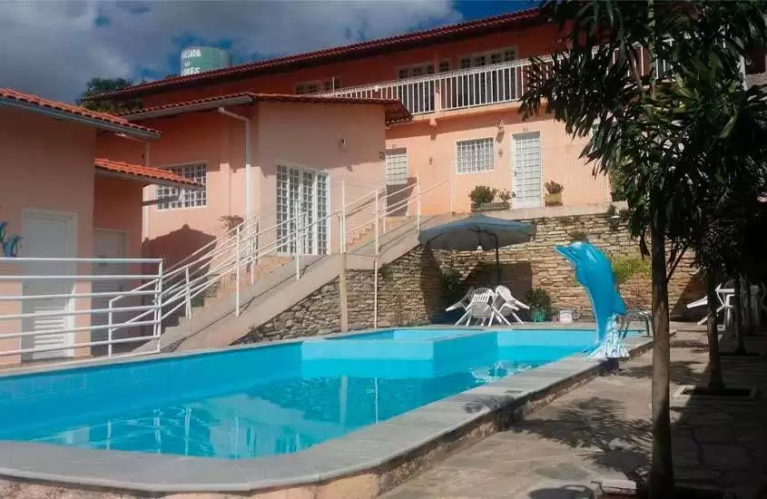 Em um dia de sol com nuvens, área de lazer de um dos hotéis fazenda próximo a brasilia com piscina, mesas, cadeiras, guarda-sóis e hotel ao lado
