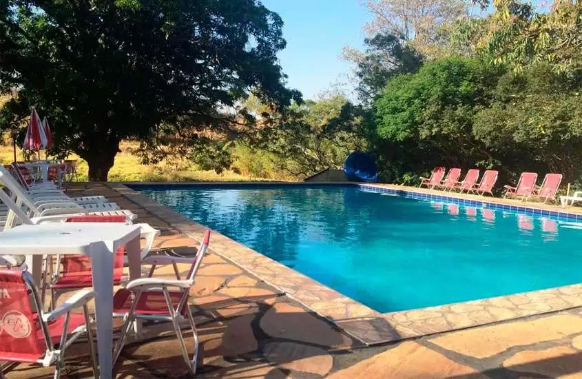 Em um dia de sol, área de lazer de um dos hotéis fazenda próximo a brasilia com mesas, cadeiras, guarda-sóis, espreguiçadeiras, piscina, árvores e parte gramada