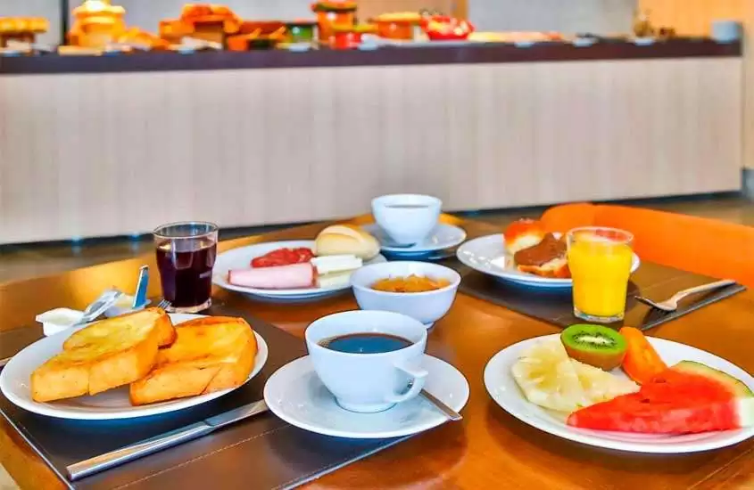 Mesa de café da manhã posta com pães, café, frutas, sucos, frios e bolos