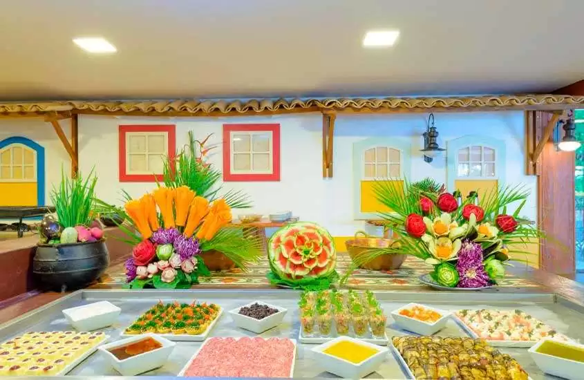 Mesa de café da manhã de um dos hotéis fazenda próximo a brasilia com furtas, frios, comidinhas, flores decorativas e parede decorada com pinturas coloridas