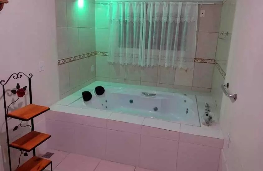 Área de banheira com estante e janela acortinada de uma pousada com hidro em penedo