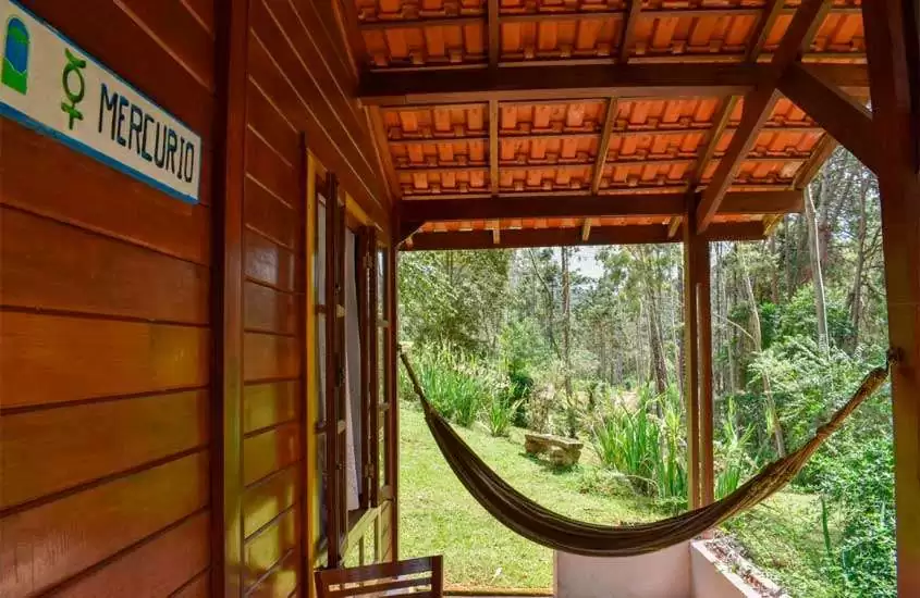 Em um dia de sol, varanda de um Hotel Fazenda na Serra da Mantiqueira com rede, estrutura de madeira e natureza ao redor