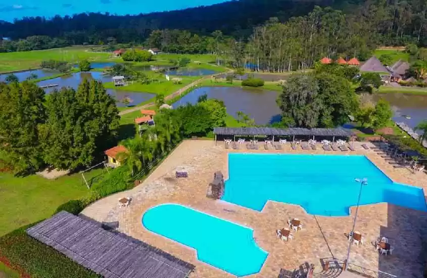 Em um dia de sol vista aérea de hotel fazenda no rio grande do sul com piscinas grandes, lagos e área verde com várias árvores ao redor