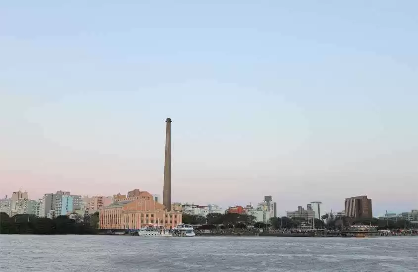 Em um fim de tarde, paisagem de Porto Alegre, um lugar barato para passar o ano novo, com prédios, construções e mar com barcos na frente