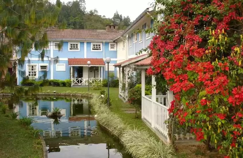 Em um dia nublado, hotel em Penedo com lago na frente casinhas coloridas e plantas ao redor