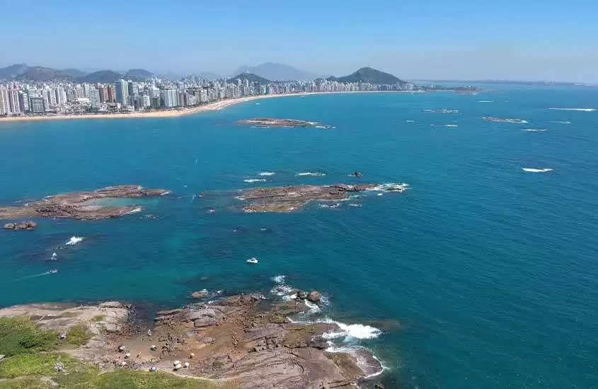 Em um dia de sol, vista aérea de Vila Velha, um dos lugares baratos para passar o ano novo com a cidade no fundo o mar no meio e pequenas ilhas de pedra