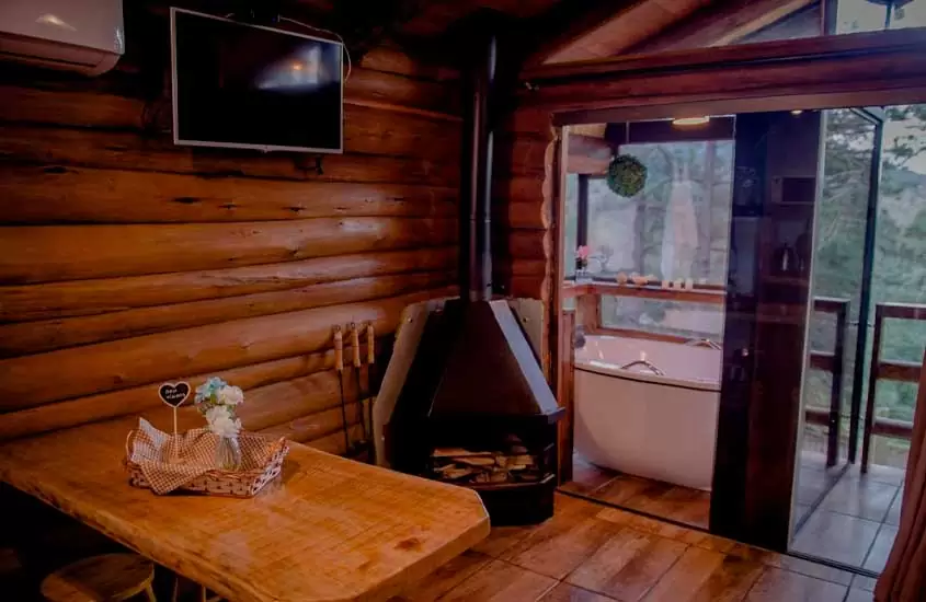 Interior de um dos chalés na serra gaúcha com lareira, banheira, moveis de madeira, ar condicionado, TV e varanda