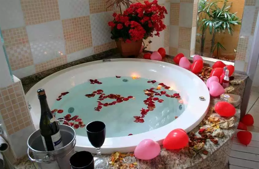 Área de banheira de um hotel para lua de mel no interior de sp com balões, flores, balde de champagne com taças e janela