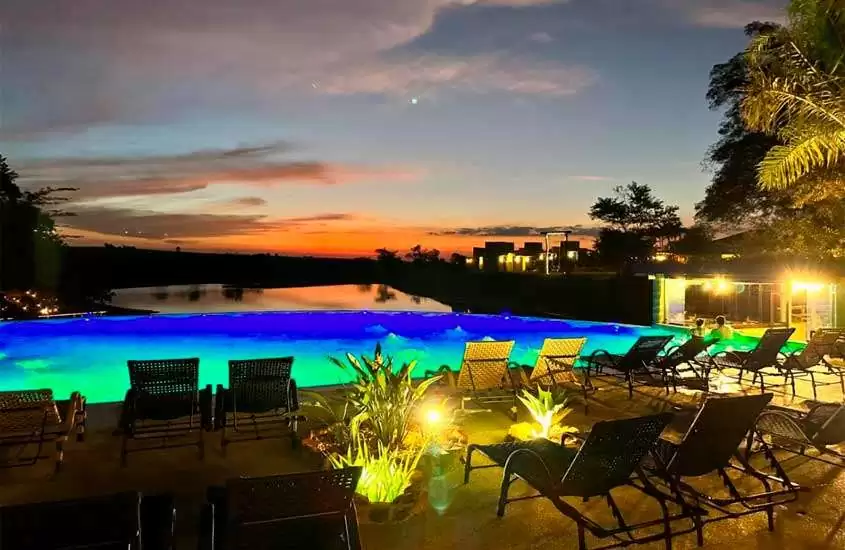 Durante o pôr do sol, área de lazer de um hotel com piscina, espreguiçadeiras, plantas e árvores decorativas
