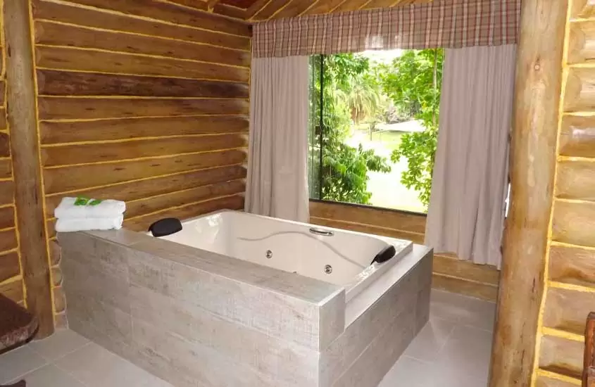 Área de banheira com janelas grandes e paredes e madeira de pousada com hidro em penedo