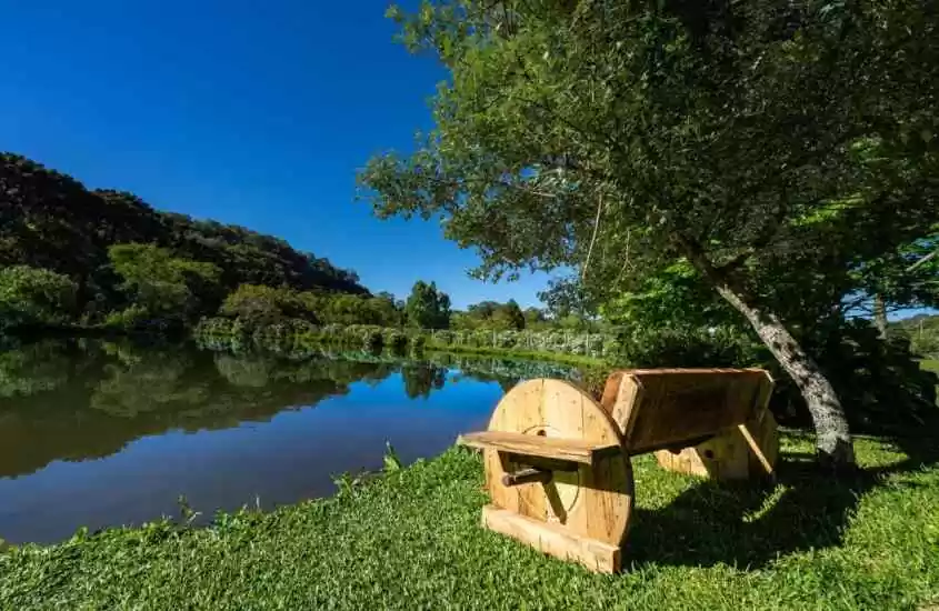 Em um dia ensolarado, banco de madeira em frente a um lago com grande área vede ao redor