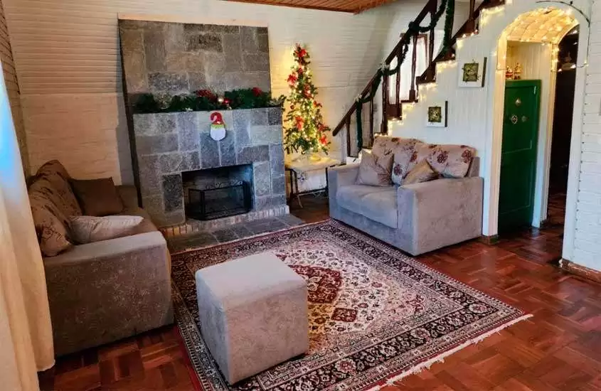 Sala de um chalé com tapete, sofás, lareira, decoração de natal, cofre e puff