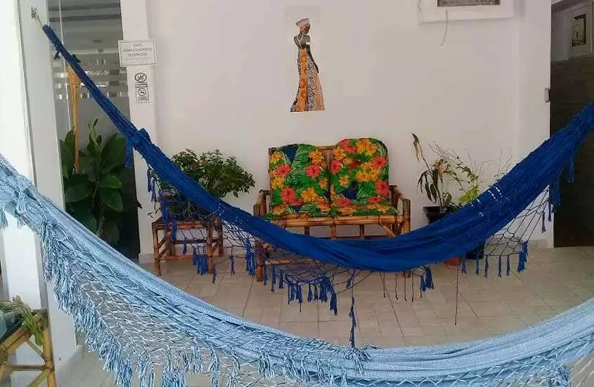 Área de descanso com redes, sofá, quadro decorativo e plantas ao redor