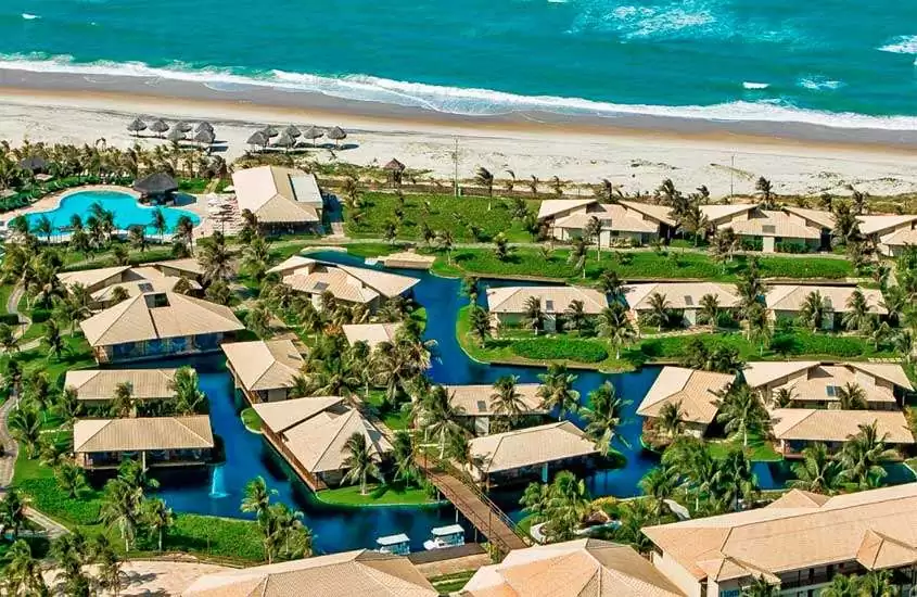 Em um dia ensolarado, vista aérea de um resort para o carnaval com piscinas, acomodações, árvores ao redor, parte gramada e praia na frente