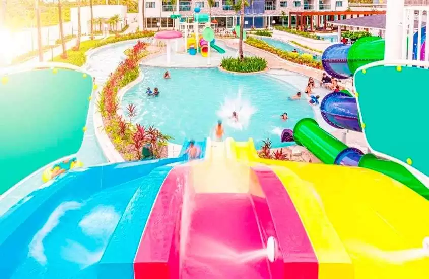 Durante uma manhã ensolarada, área de lazer de um resort para o carnaval com piscinas, brinquedos aquáticos, plantas e árvores decorativas