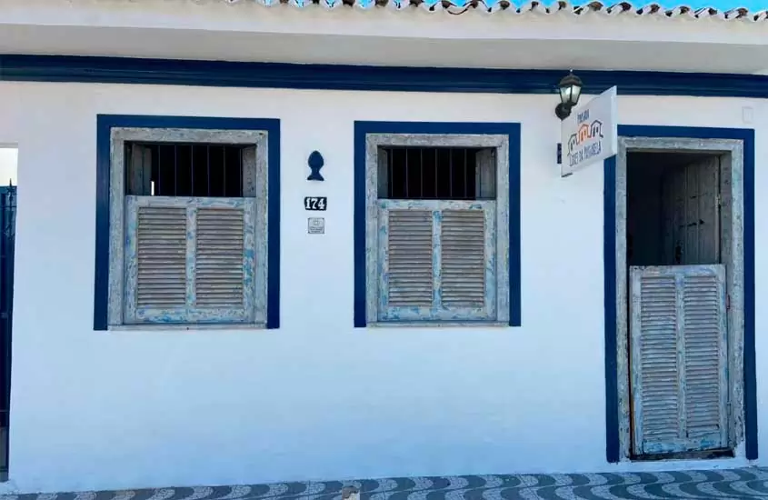 Fachada de uma das pousadas em Porto Seguro Bahia com preços baixos, placa com o nome, pintura branca e molduras azuis